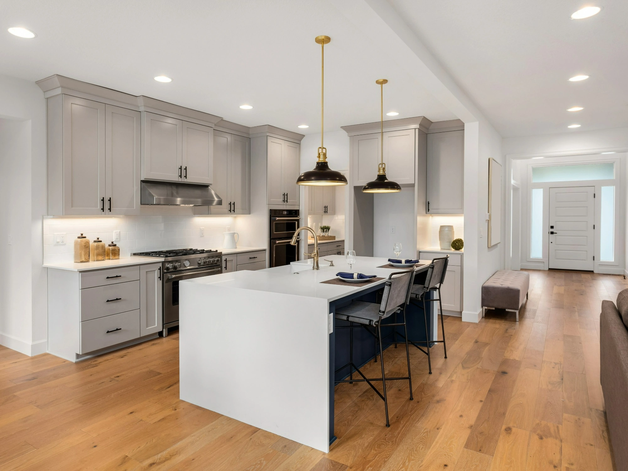 An open, white kitchen with wooden flooring and a white, rectangular island.
