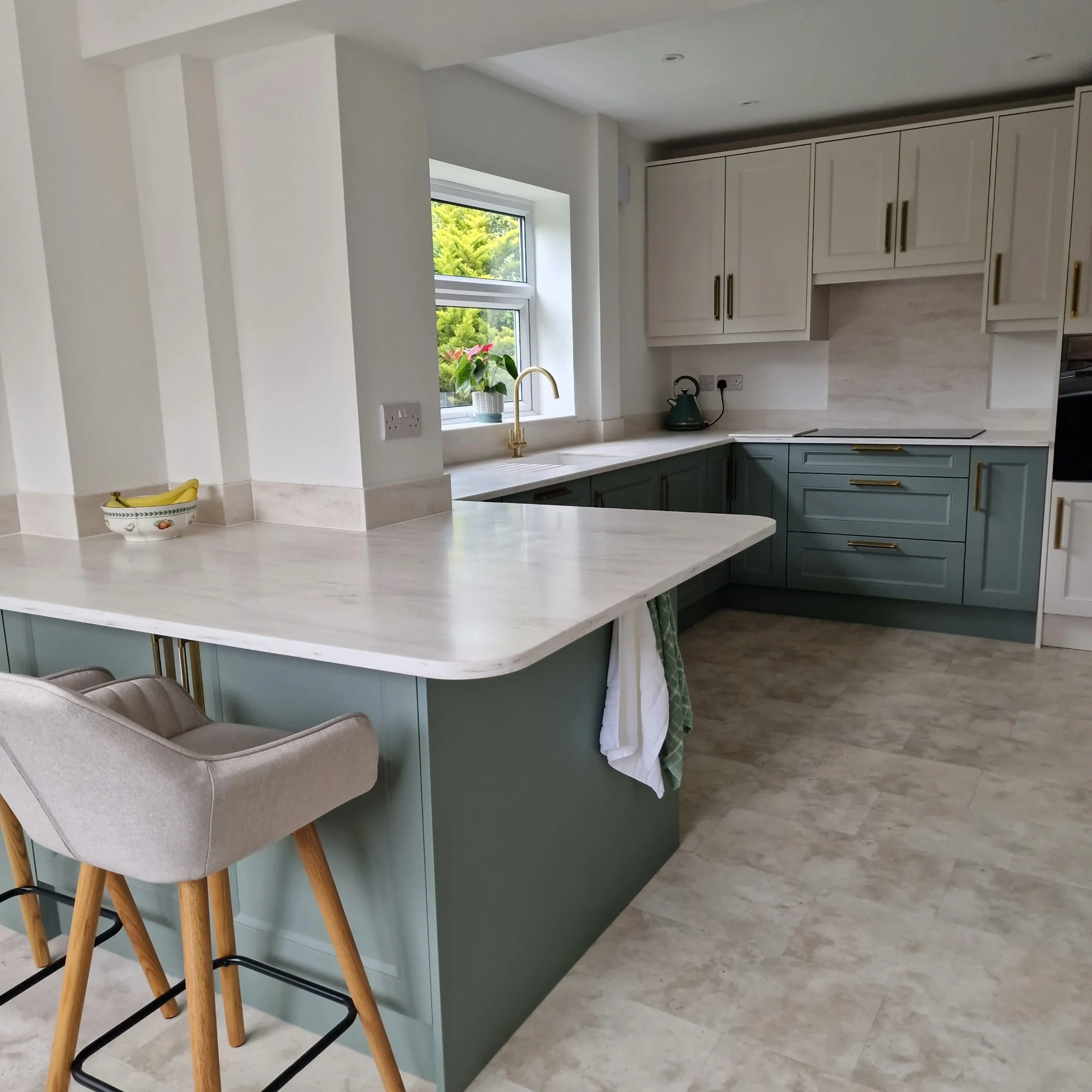 Kitchen by Premier Crafts featuring white marble countertops and teal shaker cabinets.
