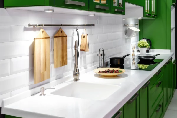 A kitchen with green cabinetry and white acrylic countertops with a sink cut into the design.