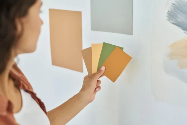 Hand of young woman with palette of colour swatches choosing one for walls of her bedroom.