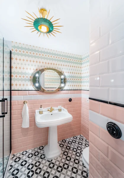 A retro bathroom featuring pink and white subway tiles, a pedestal sink, and a unique, sunburst-style light fixture.