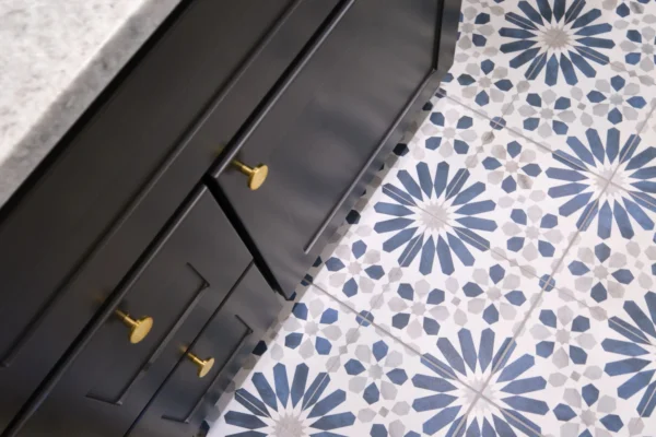 A close-up of a bathroom floor with blue and white patterned tiles next to dark cabinets with gold handles.