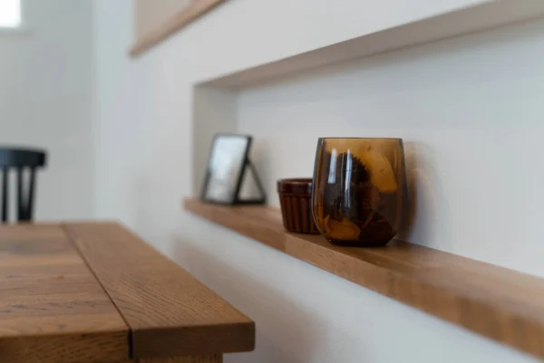 A sleek, light wooden shelf integrated into a white wall in a kitchen.