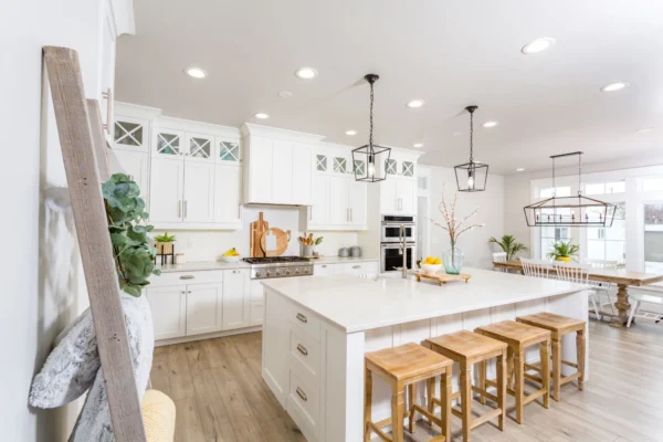 A traditional white farmhouse kitchen with oak accessories and chairs.