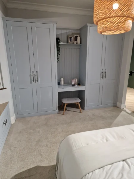 A bedroom with light blue built-in wardrobes and a central dressing table nook with a stool.
