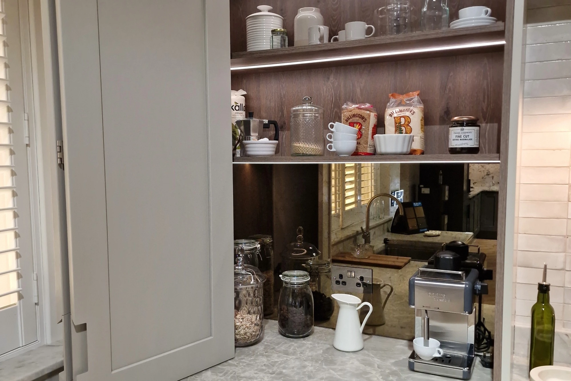A built-in storage unit in a kitchen filled with drinksware and a coffee machine.