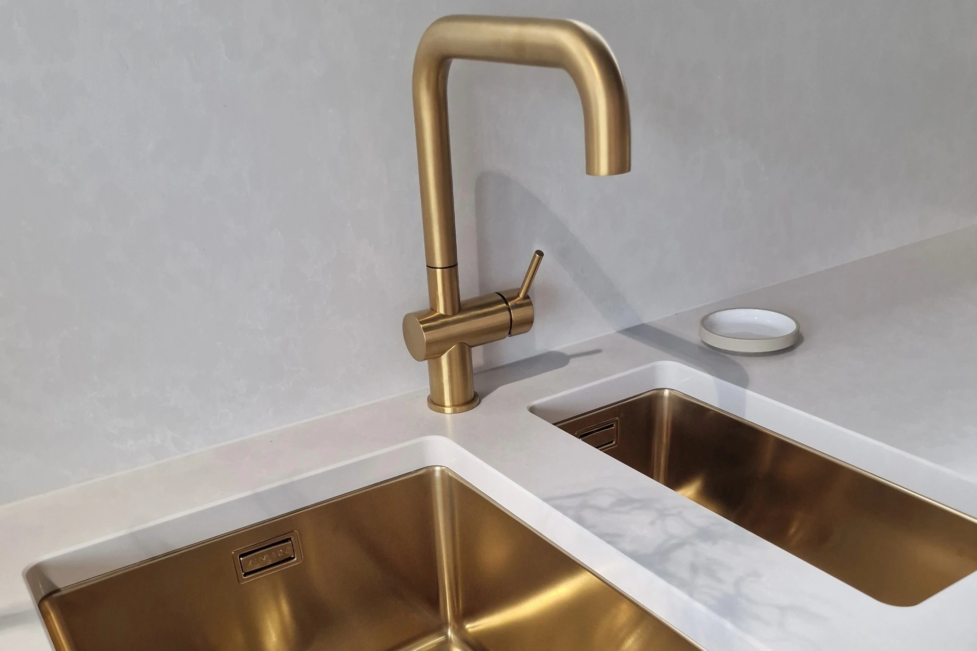 A brushed gold tap and matching sink in a modern white kitchen.