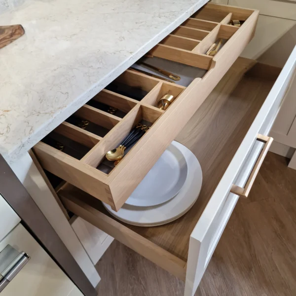 A wooden kitchen drawer pulled out, displaying plates and gold cutlery.