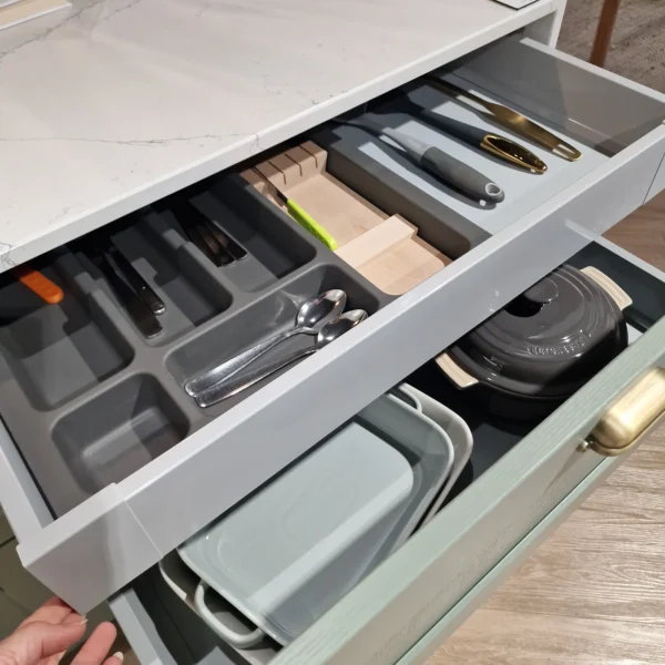 Green and grey kitchen drawers filled with pots, trays and cutlery.