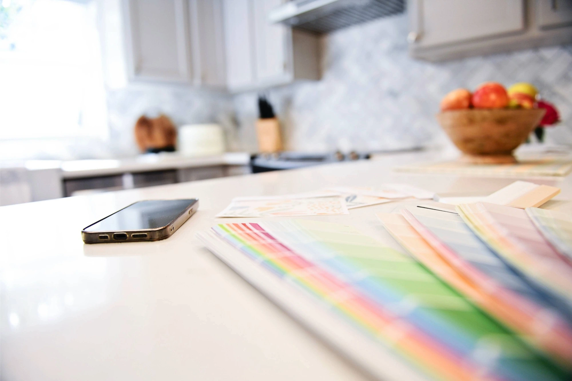 A smartphone charges on a white kitchen bench next to a set of colour swatches.