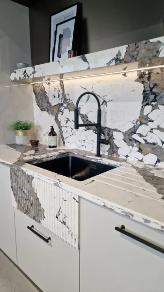 A white and grey marble-effect kitchen backwall with a black tap and basin, and the marble-effect surface continues in front of the tap, appearing as a apron.