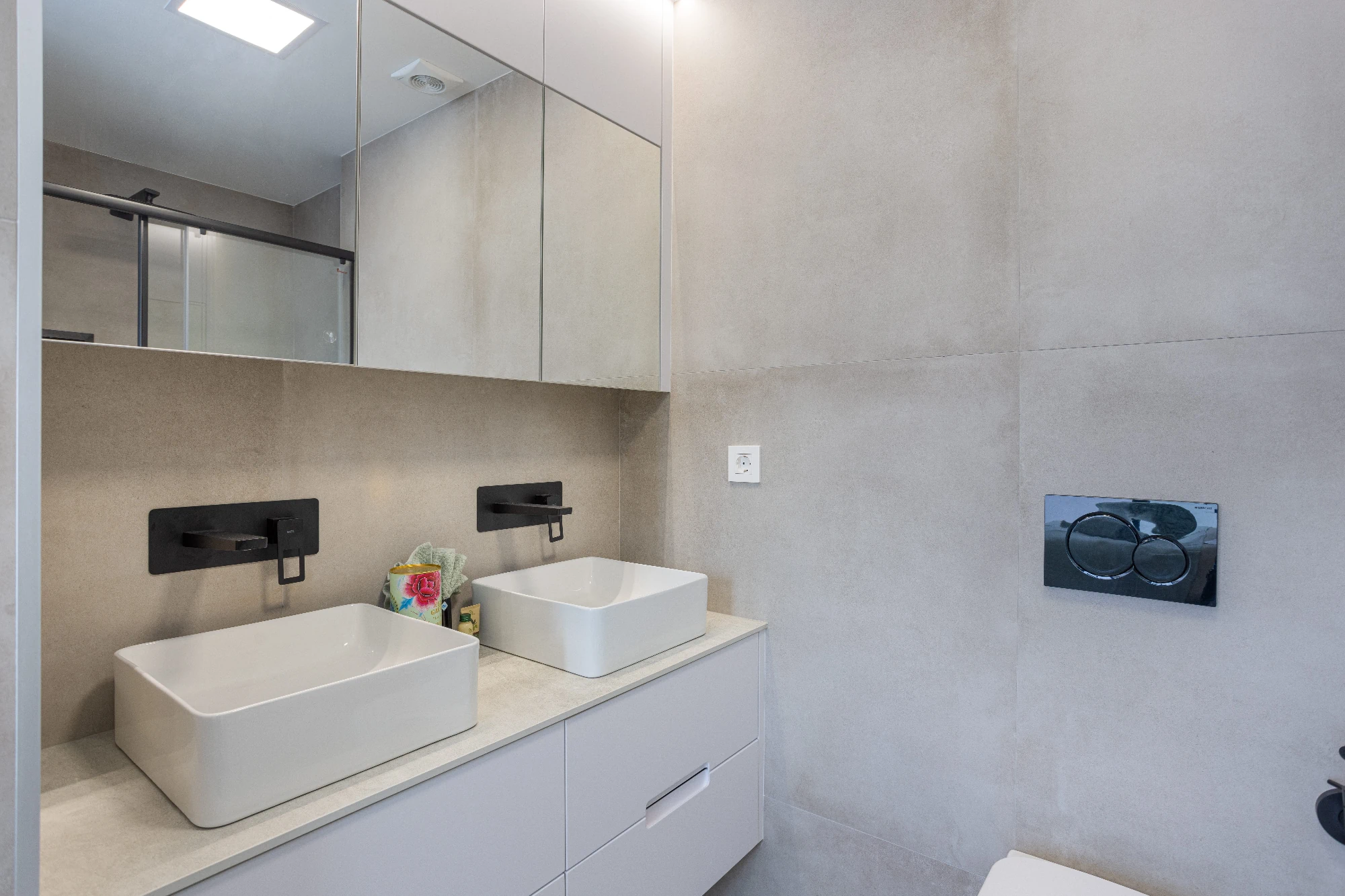 A contemporary bathroom featuring a double vanity with two square vessel sinks, black wall-mounted faucets, and a sleek mirror cabinet. 