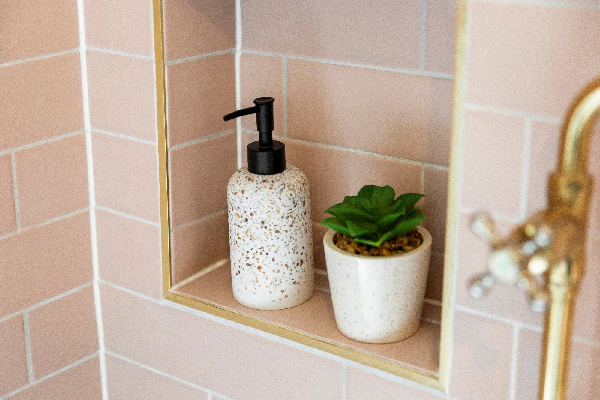 A shower niche featuring light pink ceramic tiles and gold accents.