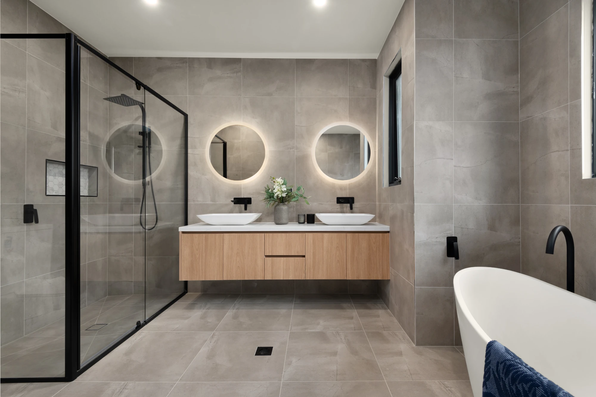 A luxurious and modern bathroom with a double vanity unit below two backlit, circular mirrors. 