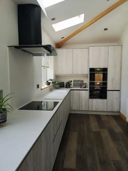 A galley kitchen with wooden features and accents. Wooden flooring and wooden, handleless cabinetry.