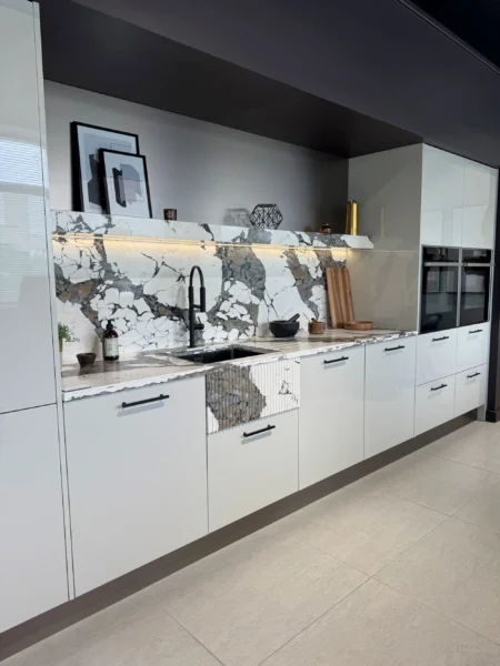 A long, narrow galley kitchen with white base cabinets, marble-effect countertops.