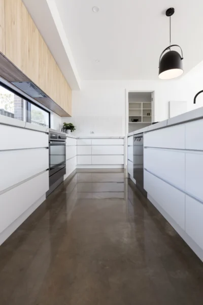 A bright, high-contrast galley kitchen with a modern design that includes white cabinets, natural wood veneer, and dark reflective flooring.