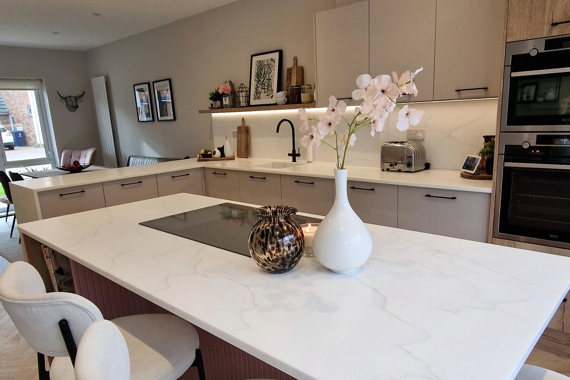 A kitchen island in a white stone finish with an integrated hob and vase of flowers on it.