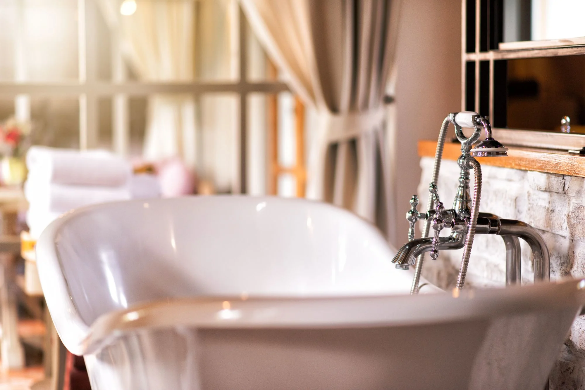 Close-up of a classic white roll-top bathtub with vintage chrome fixtures in a cosy, bright bathroom.