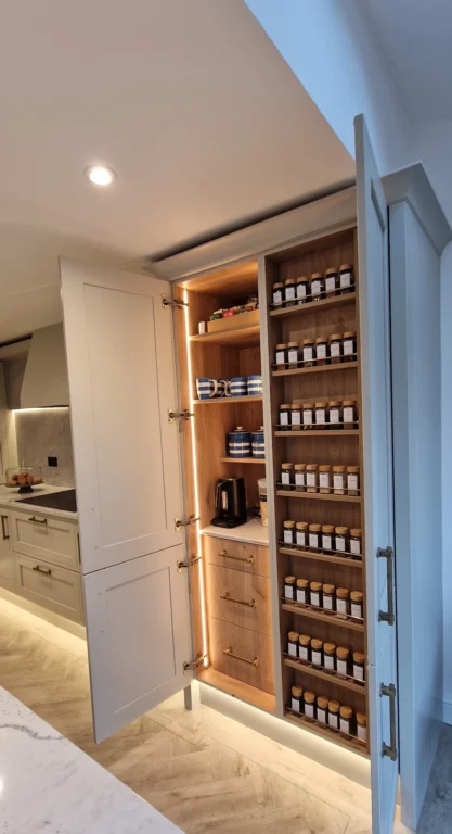 A luxuriously organised kitchen larder cabinet with built-in LED lighting, featuring wood-lined shelves for spices and integrated drawers for storage.