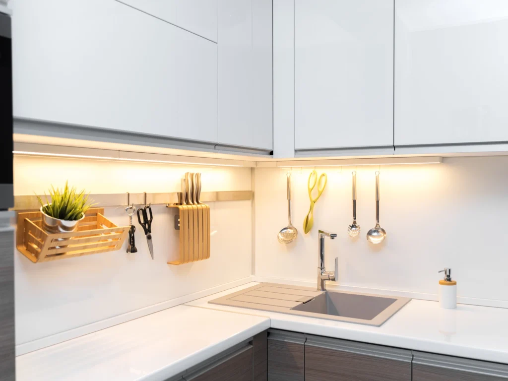 A minimalist kitchen corner featuring high-gloss white upper cabinets, dark wood lower cabinets, and warm under-cabinet LED lighting.