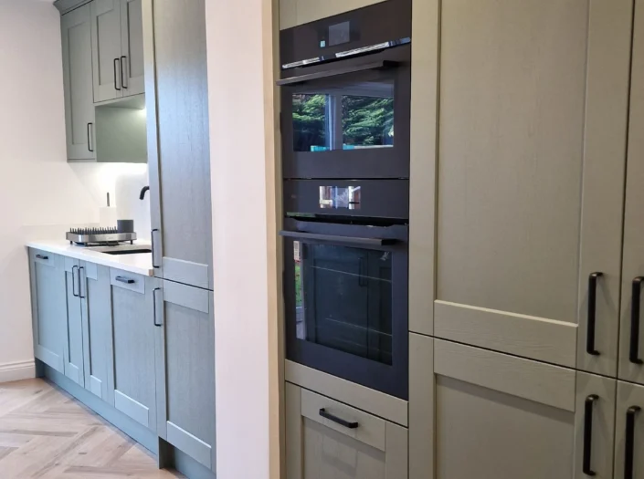 Sage green kitchen cupboards with integrated black ovens.