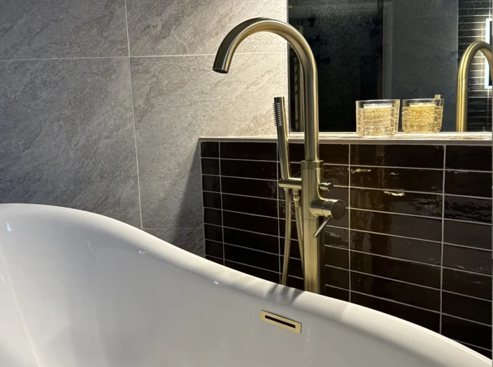 Close-up of a white freestanding bathtub featuring a floor-mounted brushed gold faucet and handheld sprayer.
