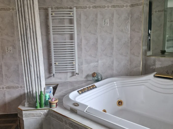 Light marble effect bathroom with large pillar and jacuzzi.