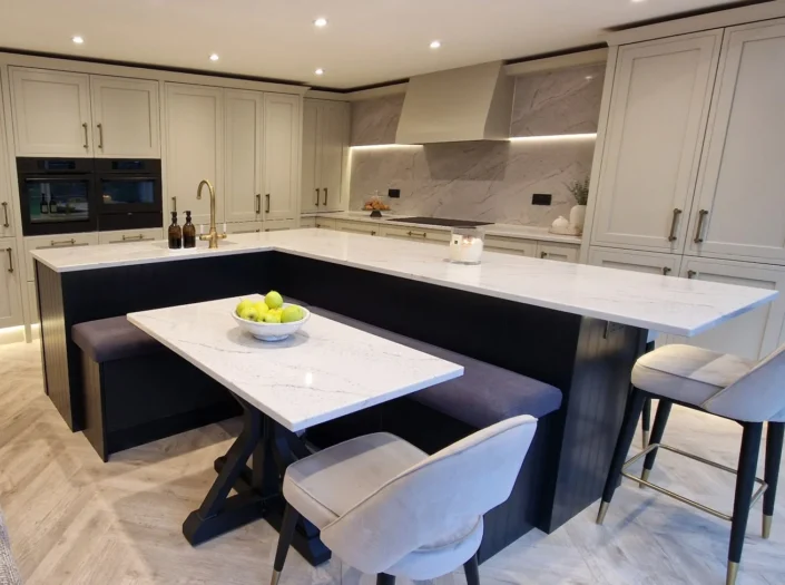 High-angle view of a contemporary kitchen showcasing a multi-functional island with integrated blue velvet banquette seating, a marble dining table, and a wall of floor-to-ceiling off-white cabinetry with gold hardware.