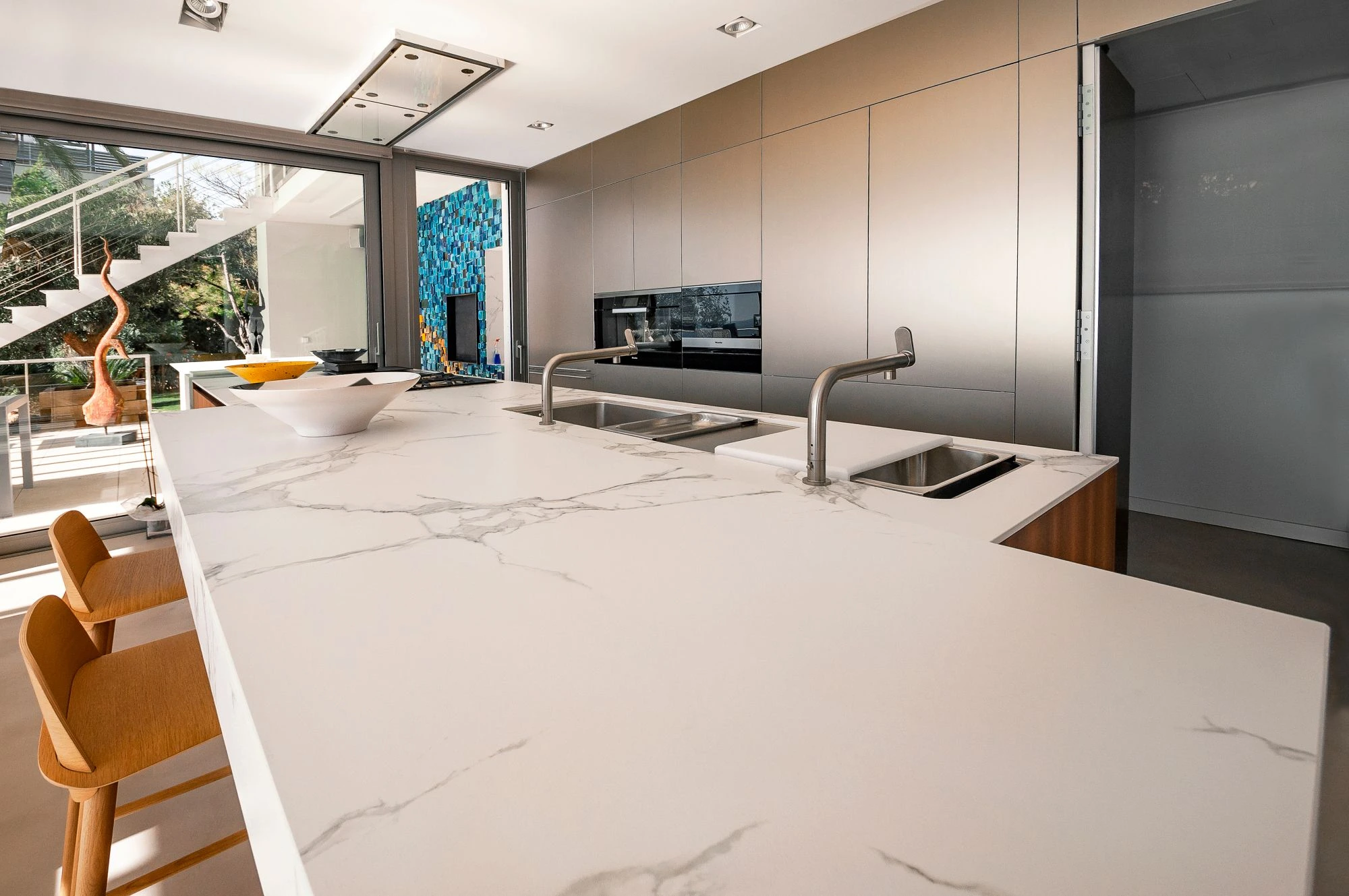 Modern minimalist kitchen with a large white marble island, integrated sinks, and sleek metallic cabinetry.