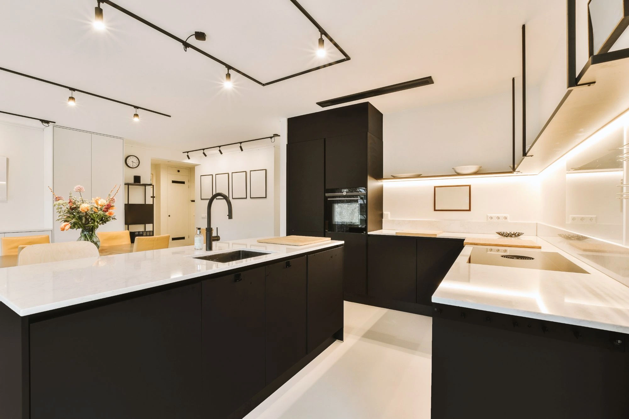 Modern black and white kitchen featuring a large black island, white countertops, and minimalist track lighting.