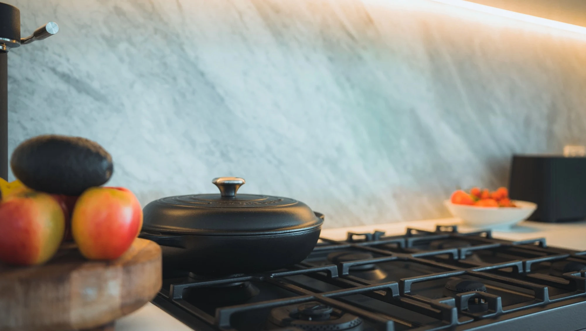 A black gas hob in front of a large natural stone backsplash.