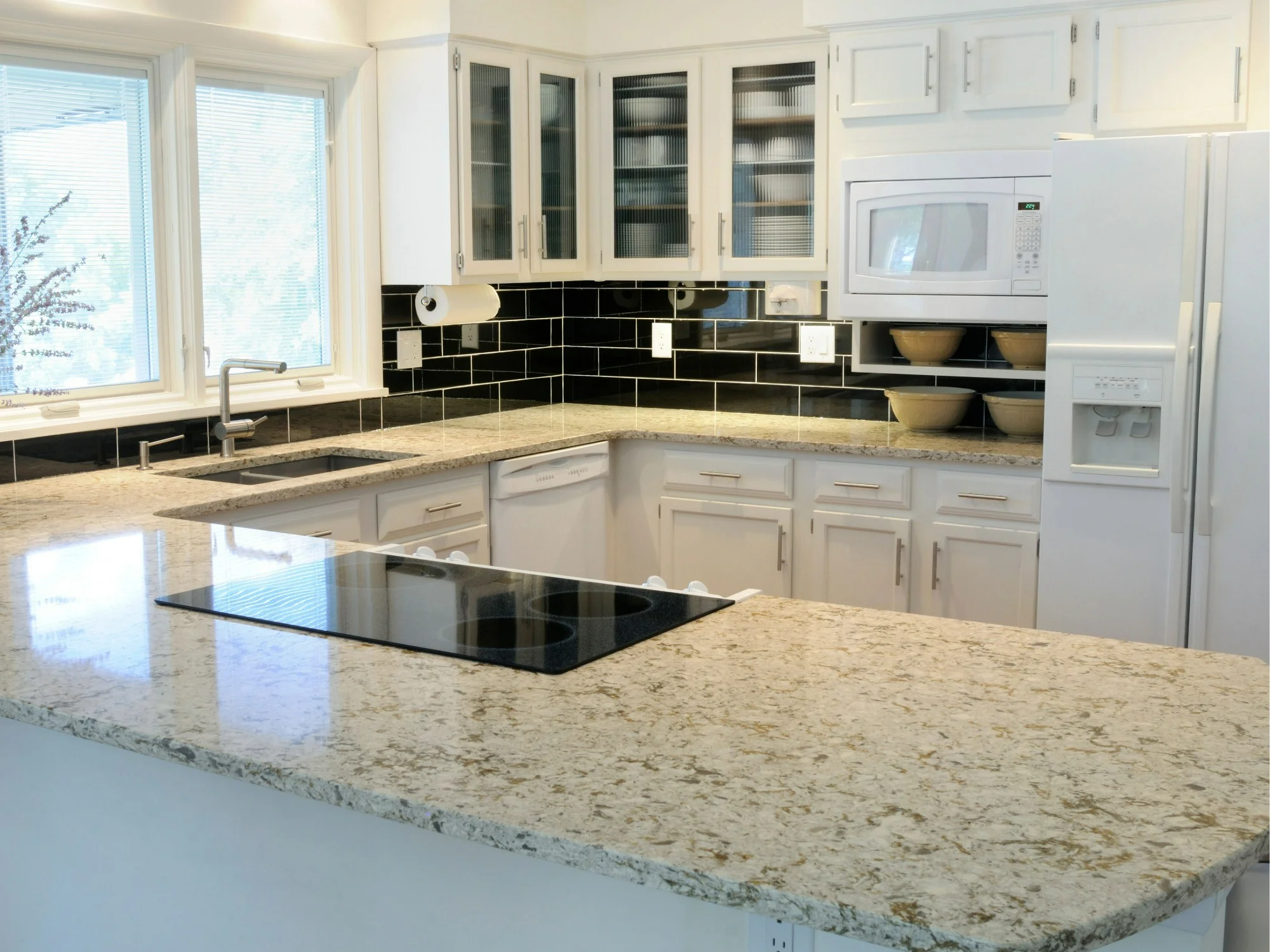 Modern white kitchen with integrated hob and granite countertops.